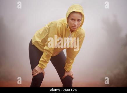 Si allena in qualsiasi tempo. Una giovane runner femminile che si ferma per un riposo mentre fuori in una corsa attraverso una foresta nebbiosa. Foto Stock