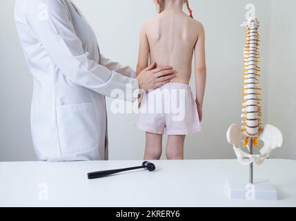 Un medico neurologo pediatrico esamina la schiena di una bambina di 5 anni che ha dolore alla schiena. Trattamento del dolore muscolare e della scoliosi nei bambini, kyphoscol Foto Stock