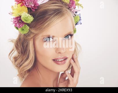 Offre una vera bellezza. Una giovane donna con un fiore arrangiato nei suoi capelli sorridendo alla macchina fotografica. Foto Stock