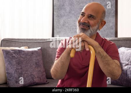 Ritratto di un uomo anziano allegro seduto con il mento appoggiato sul bastone Foto Stock