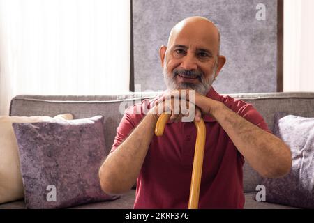 Ritratto di un uomo anziano allegro seduto con il mento appoggiato sul bastone Foto Stock