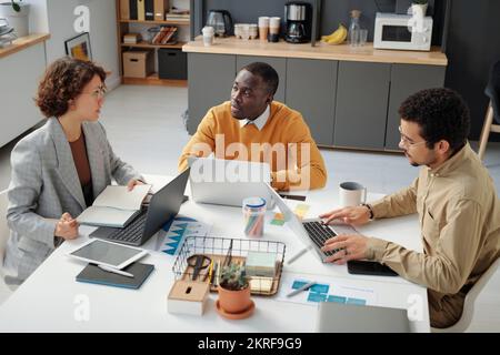 Vista ad alto angolo del gruppo di sviluppatori che lavorano con un programma informatico in team durante una riunione aziendale Foto Stock