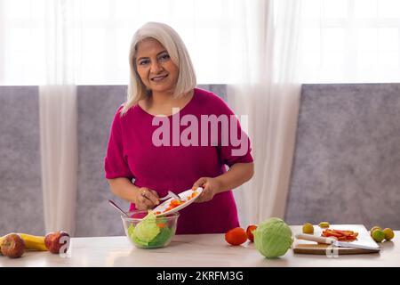 Vecchia donna che prepara insalata di verdure in cucina Foto Stock