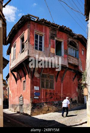 Bergama, Turchia, settembre 2018: Un vecchio che cammina in una strada con la tradizionale casa anatolica rossa nel vecchio villaggio di Pergamon Foto Stock