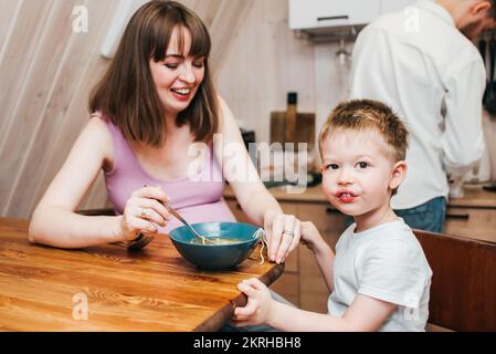Madre felice con padre che nutre il bambino in cucina con la pasta Foto Stock
