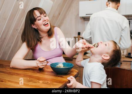 Madre felice con padre che nutre il bambino in cucina con la pasta Foto Stock