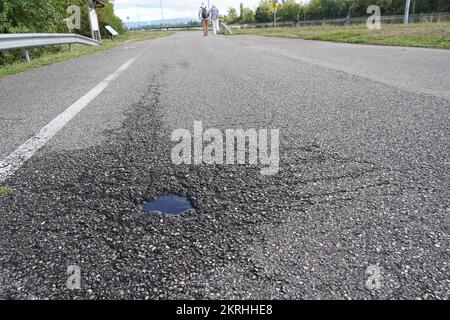 Strada asfaltata con un piccolo buche pieno di acqua piovana in vista ad angolo basso. Foto Stock