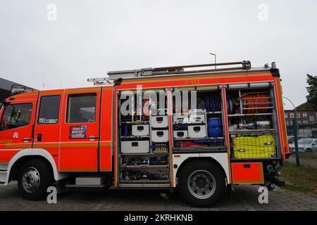 Vista sul camion dei vigili del fuoco arancione con la porta laterale aperta del luogo di stivaggio dove sono visibili le manichette antincendio. Foto Stock