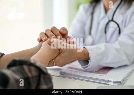 Medico senior asiatico professionale e pacifico tiene le mani della sua giovane paziente, offrendo sostegno e rassicurandola durante il controllo mediale. ritagliato Foto Stock