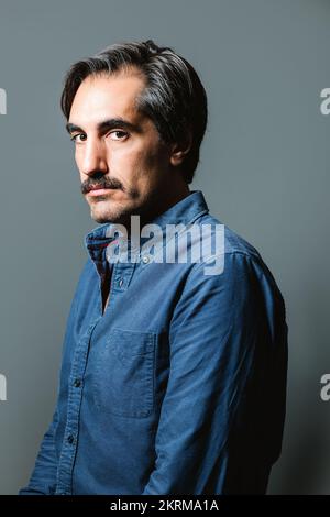 Giovane uomo sicuro in camicia blu su sfondo grigio e guardando la fotocamera Foto Stock