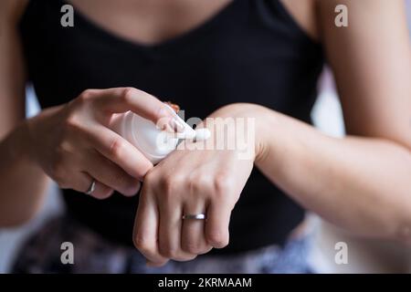 Crop anonymous etnico femmina dimostrando la crema mentre mettendo la sostanza a portata di mano dal tubo in makeup studio Foto Stock