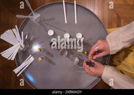 Vista dall'alto di anonimo artigiano con contagocce che fanno profumo in vaso di vetro sul tavolo a casa Foto Stock