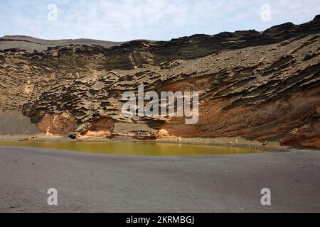 Lago Verde panoramico con sabbia vulcanica nera circondato da montagne rocciose in una giornata di sole nelle Isole Canarie Foto Stock