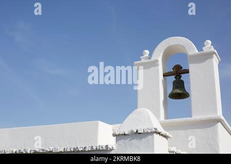 Basso angolo di facciata di vecchio edificio in pietra bianca con campana di metallo in torre ad arco sotto cielo blu senza nuvole Foto Stock
