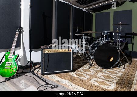 Altoparlante professionale con filo su tappeto vicino a batteria e chitarre in studio di registrazione per performance musicali Foto Stock