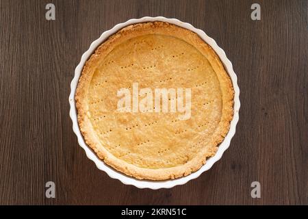 Una sfoglia di pasta frolla cotta cieca in una teglia/quiche di ceramica bianca, pronta per il ripieno. Concetto - preparazione alimentare Foto Stock