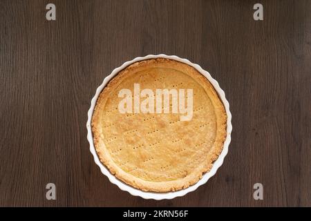 Una sfoglia di pasta frolla cotta cieca in una teglia/quiche di ceramica bianca, pronta per il ripieno. Con spazio di copia. Concetto - preparazione alimentare Foto Stock