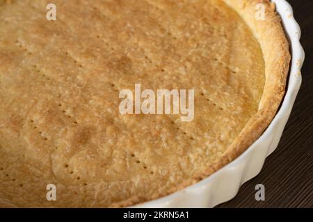 Una sfoglia di pasta frolla cotta cieca in una teglia/quiche di ceramica bianca, pronta per il ripieno. Concetto - preparazione alimentare Foto Stock