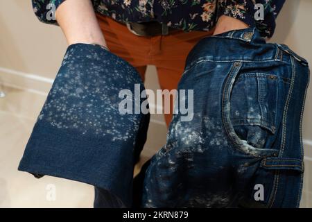 Donna in possesso di un paio di jeans con muffa bianca crescere su di loro a causa di umidità e condensa. Concetto: Problemi di noleggio in un appartamento britannico, ventilazione scarsa, Foto Stock