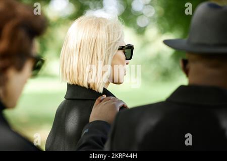 Vista laterale della giovane donna che indossa occhiali da sole scuri durante la cerimonia funeraria all'aperto Foto Stock