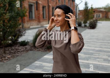 Una donna adulta ama ascoltare la musica preferita con le cuffie wireless in mezzo alla strada Foto Stock