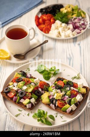 Gustosi e sani avocado, olive, pomodori ciliegini e sandwich al formaggio feta. Tostatura con avocado, pomodori e feta. Foto Stock