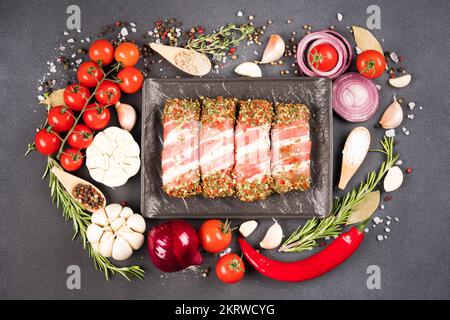 Balcanico cevapcici o romeno mitigei su piatto nero. Cibo tradizionale balcanico. Involtini di carne cruda macinata avvolti con pancetta con condimento e verdure a Foto Stock