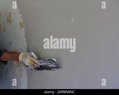 finitura livellare la superficie della parete della stanza con un'ampia spatola, coprendo la parete con uno strato uniforme di stucco con forti movimenti della lastra Foto Stock