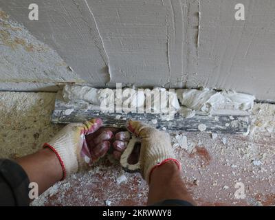 applicare lo stucco sulla parete con una spatola larga, livellando la parete con l'intonaco di finitura dal basso verso l'alto utilizzando una cazzuola larga Foto Stock