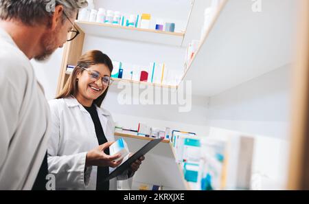 Farmacisti che raccolgono farmaci da uno scaffale in un chimico. Due professionisti sanitari maturi che elaborano prescrizioni online in farmacia. Foto Stock