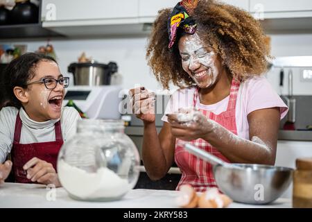 Mamma e figlia giocano con la farina mentre preparano dolci a casa, momenti di divertimento e di gioco tra genitori e figlie in cucina Foto Stock