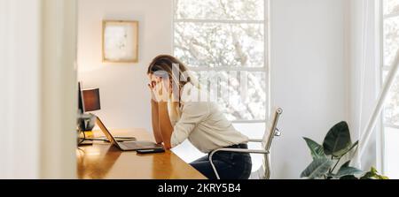 Donna d'affari sovraccarica che ha un mal di testa nel suo ufficio. Una donna d'affari sopraffatta che si trova davanti a un notebook e si trova in una situazione di fatica lavorativa. Foto Stock