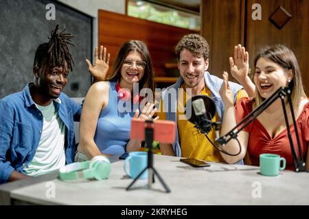 momento di saluto durante una trasmissione di video influencer, quattro giovani studenti utilizzano uno smartphone e collegamenti wireless per creare contenuti online su socia Foto Stock