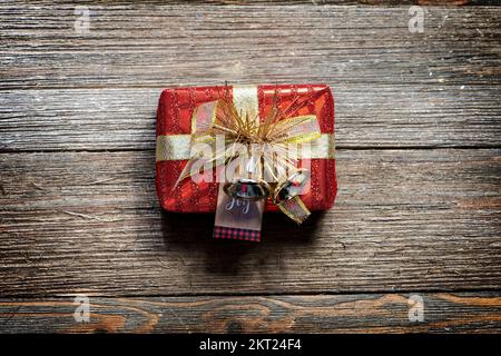 Piccola scatola regalo rossa e dorata su uno sfondo rustico in legno, in stile casale. Foto Stock