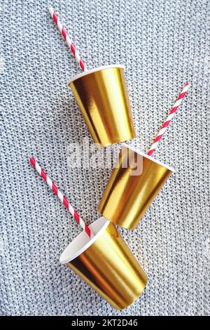 Coppe in carta color oro con paglia a righe su fondo lavorato a maglia per le decorazioni delle feste di Natale Foto Stock