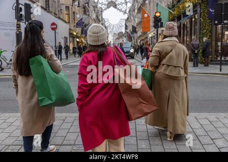 Gli amanti dello shopping natalizio nel centro di Londra con colorati cappotti invernali e borse per lo shopping a Piccadilly, nel centro di Londra, Inghilterra, Regno Unito Foto Stock