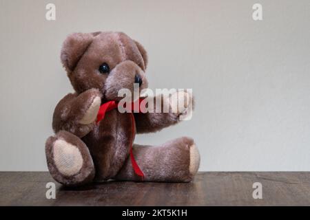 Primo piano di un grazioso orsacchiotto marrone seduto con nastro rosso isolato su sfondo chiaro Foto Stock