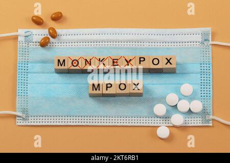 Le parole Monkeypox e Mpox sono disposte con cubi di legno su una maschera chirurgica. MPOX è il nuovo nome per il virus monkeypox. Foto Stock