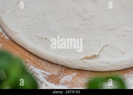 Preparare la pasta per la pizza su un asse di legno con farina bianca e ingredienti intorno, primo piano, spazio copia Foto Stock