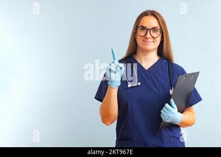 Medico donna con stetoscopio e clipboard puntando il dito verso l'alto Foto Stock