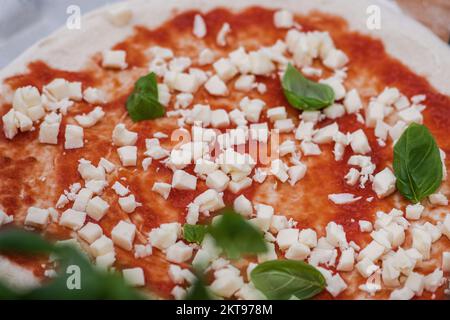 Preparare la pizza con salsa di pomodoro, mozzarella fresca e foglie di basilico verde su un asse di legno, primo piano Foto Stock