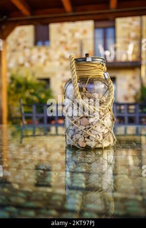 Vaso di vetro con pietre sulla parte superiore di un rustico tavolo casa di campagna. Foto Stock