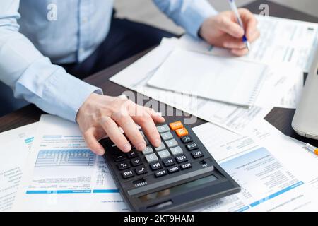 Uomo d'affari che utilizza la calcolatrice per calcolare le fatture al tavolo in ufficio Foto Stock