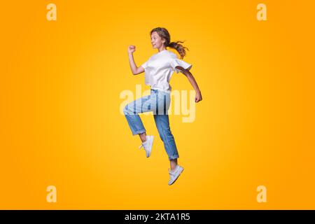 Profilo a lunghezza intera foto di divertente giovane donna che corre veloce in vendita indossando giacca, jeans e sneakers isolato su sfondo giallo. Giallo Foto Stock
