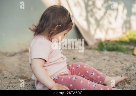 Bambina che esplora un mucchio di sabbia, la tocca, raccoglie la sabbia in un pugno, studia il materiale naturale. Stile di vita delle persone. Sano attivo Foto Stock