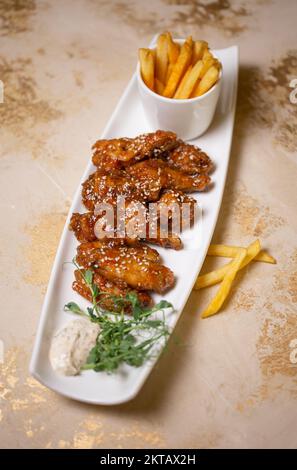 ali in salsa agrodolce con semi di sesamo e patatine fritte su un piatto bianco. Foto Stock