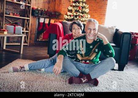 Ritratto completo di due persone anziane soddisfatti allegre sedersi tappeto pavimento coccole fata christmastime miracolo al coperto Foto Stock