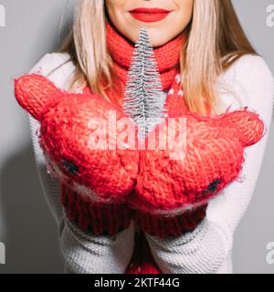 Ragazza che tiene il piccolo albero di Natale. Isolare su grigio. Foto Stock