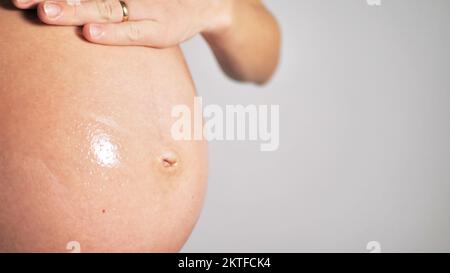 La giovane donna incinta sfrega l'olio di massaggio nel ventre. Cura della pelle addominale durante la gravidanza. Cosmetici naturali. Salute di una donna incinta Foto Stock