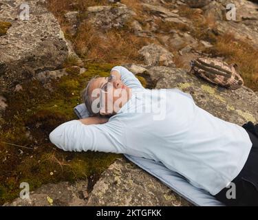 Primo piano ritratto di una donna dai capelli grigi che giace su una pietra, guarda nel cielo. Foto di alta qualità Foto Stock